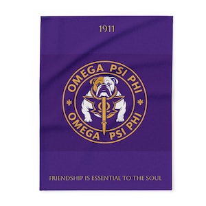 May include: A purple blanket featuring the Omega Psi Phi fraternity crest in gold and white. The crest includes a bulldog, the Greek letters, and the year 1911. The text "Friendship is essential to the soul" is at the bottom.