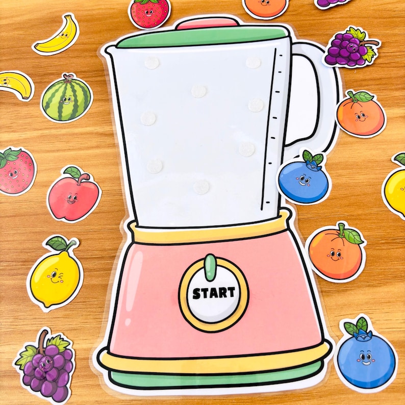 May include: A colorful illustration of a blender with the word "START" on the front. The blender is pink, white, and green, surrounded by cartoon fruit stickers including strawberries, blueberries, and oranges. The stickers are on a wooden surface.