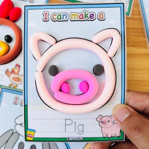 Puede incluir: Un proyecto de manualidades para ni&ntilde;os con un cerdo hecho de arcilla rosa y rosa claro sobre una tarjeta. La tarjeta tiene el texto "I can make a" en la parte superior y "Pig" en la parte inferior, con una ilustraci&oacute;n de cerdo de dibujos animados. El logotipo de Play-Doh es visible.