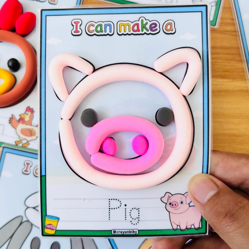 Puede incluir: Un proyecto de manualidades para ni&ntilde;os con un cerdo hecho de arcilla rosa y rosa claro sobre una tarjeta. La tarjeta tiene el texto "I can make a" en la parte superior y "Pig" en la parte inferior, con una ilustraci&oacute;n de cerdo de dibujos animados. El logotipo de Play-Doh es visible.