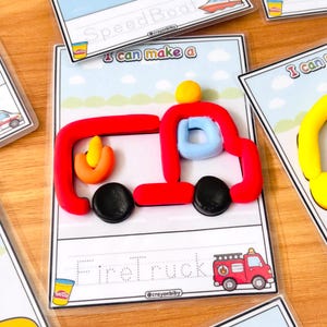 Op de afbeelding: Een rode, blauwe, gele en zwarte klei brandweerwagen op een witte achtergrond met de woorden "Firetruck" en "I can make a" op de kaart. De kaart heeft ook een kleine illustratie van een brandweerwagen.