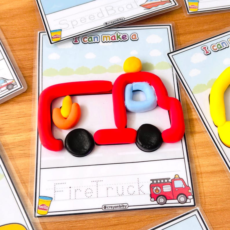 Op de afbeelding: Een rode, blauwe, gele en zwarte klei brandweerwagen op een witte achtergrond met de woorden "Firetruck" en "I can make a" op de kaart. De kaart heeft ook een kleine illustratie van een brandweerwagen.