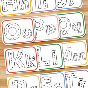Puede incluir: Un conjunto de tarjetas educativas con letras may&uacute;sculas y min&uacute;sculas del alfabeto. Cada tarjeta blanca tiene un borde de color y muestra una letra grande con l&iacute;neas discontinuas y flechas numeradas que indican el orden de trazo correcto.