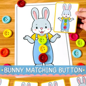 Pode incluir: Um jogo de correspondência de botões com um coelho de desenho animado vestindo jardineiras azuis num cartão branco. Três botões coloridos em verde-lima, amarelo e vermelho estão colocados no peito do coelho. Inclui um cartão de referência.
