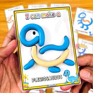 Puede incluir: Un rompecabezas de plesiosaurio azul y crema con el texto "I can make a" en la parte superior. El rompecabezas est&aacute; en una funda de pl&aacute;stico transparente. Un plesiosaurio de dibujos animados est&aacute; en la esquina inferior derecha.
