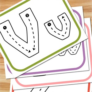 Puede incluir: Una pila de tarjetas educativas que muestran la letra V en may&uacute;scula y min&uacute;scula. Cada letra est&aacute; delineada en negro con l&iacute;neas discontinuas y flechas numeradas que indican el orden de los trazos para escribir. Las tarjetas tienen bordes de colores.