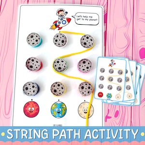 May include: A space-themed string path activity board featuring a cartoon astronaut on a rocket with the text Let's help me get to my planet. The board includes moon-shaped pegs, a yellow string, and a stack of matching task cards.