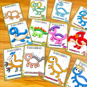 Puede incluir: Un conjunto de tarjetas de manualidades con tem&aacute;tica de dinosaurios. Cada tarjeta presenta un dinosaurio diferente, como un Braquiosaurio o un Velociraptor, con la frase "I can make a" impresa. Los dinosaurios est&aacute;n hechos de arcilla colorida.