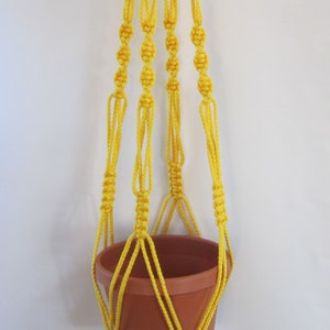 May include: A yellow macrame plant hanger with a terracotta pot. The hanger is made with a thick cord and has a tassel at the bottom.