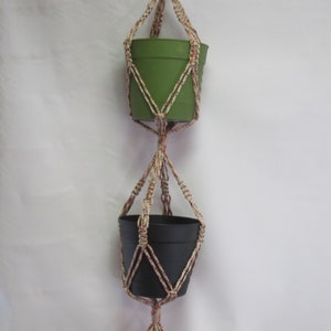 May include: A macrame plant hanger with three pots. The top pot is green, the middle pot is black, and the bottom pot is brown. The hanger is made with white and brown twine.