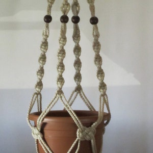 May include: A macrame plant hanger with a brown terracotta pot. The hanger is made of natural white cotton cord and has four wooden beads.