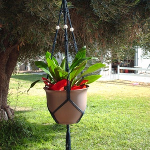 May include: A dark blue macrame plant hanger with white beads, holding a brown pot with a green plant and red flowers.