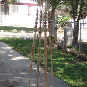 May include: A macrame plant hanger with a terracotta pot. The hanger is made of natural twine and has a simple design. The pot is empty and ready for a plant.