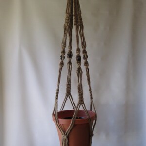 May include: A macrame plant hanger with brown beads and a terracotta pot.