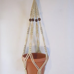 May include: A macrame plant hanger with a terracotta pot. The hanger is made of natural cream-colored cord and has wooden beads.