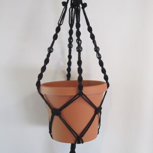 May include: Black macrame plant hanger with wooden beads and a terracotta pot.