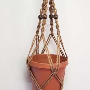 May include: A brown macrame plant hanger with wooden beads and a terracotta pot.