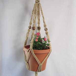 May include: A macrame plant hanger with wooden beads, holding a terracotta pot with a small pink flowering plant.