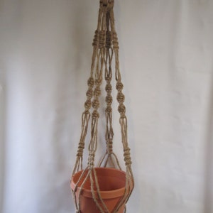 May include: A macrame plant hanger made of natural jute rope with a terracotta pot hanging from it. The hanger has a knotted design and is perfect for adding a touch of bohemian style to your home.