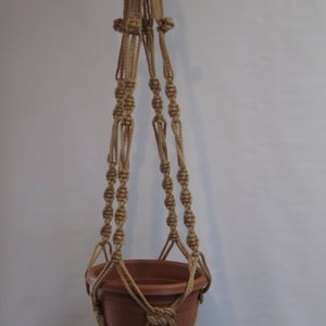 May include: A macrame plant hanger made of natural jute rope with a terracotta pot. The hanger has a simple design with a tassel at the bottom.