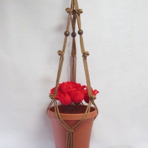 May include: A brown macrame plant hanger with wooden beads, holding a terracotta pot with red flowers.