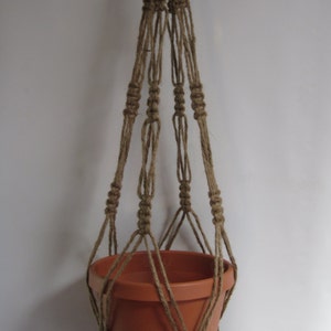 May include: A brown macrame plant hanger with a terracotta pot. The hanger is made of natural fiber rope and has a tassel at the bottom.