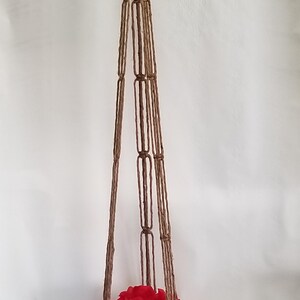 May include: A brown macrame plant hanger with a terracotta pot and red silk flowers.