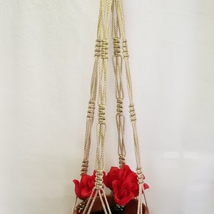 May include: A macrame plant hanger with a terracotta pot and red flowers. The hanger is made of natural beige rope and has a simple design.