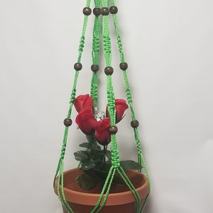 May include: Green macrame plant hanger with wooden beads and a terracotta pot with red flowers.