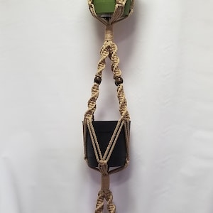 May include: Three hanging plant macrame planters with brown wooden beads. The top planter is green, the middle planter is black, and the bottom planter is brown.