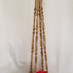 May include: A brown macrame plant hanger with a terracotta pot and a red flower inside. The hanger is made of thick rope and has a knotted design.