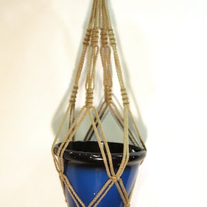 May include: A macrame plant hanger made of natural jute rope with a blue and black ceramic pot hanging from it.