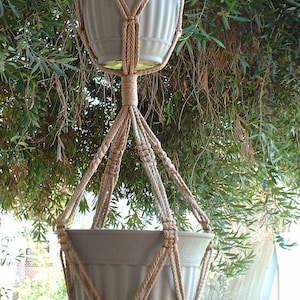 May include: A macrame plant hanger with two white ceramic pots. The hanger is made of natural brown rope and has a tassel at the bottom.