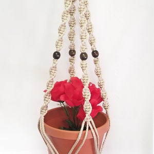 May include: A beige macrame plant hanger with wooden beads and a terracotta pot with red flowers.