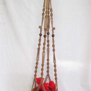 May include: A brown macrame plant hanger with wooden beads and a terracotta pot with red flowers.