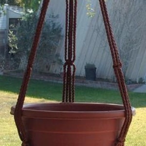May include: A brown macrame plant hanger with a terracotta pot. The hanger is made of thick rope and has a tassel at the bottom.