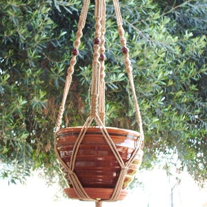 May include: A macrame plant hanger with a brown terracotta pot. The hanger is made of natural twine and has wooden beads.