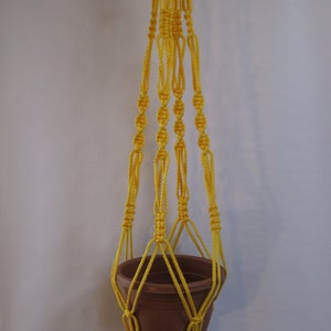 May include: A yellow macrame plant hanger with a brown terracotta pot.