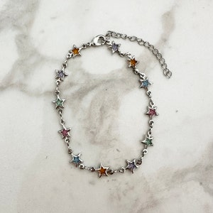 May include: A silver chain bracelet with a star charm design. Each star has a different coloured enamel fill, including pink, blue, green, and orange.