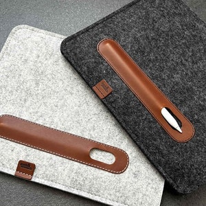 May include: Two felt iPad cases with a brown leather pen holder. The case on the left is light gray and the case on the right is dark gray.