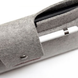 K&ouml;nnte beinhalten: Ein graues Filz-Etui mit einem schwarzen Tablet und einem wei&szlig;en Stift im Inneren. Das Etui hat einen Druckknopfverschluss und einen kleinen Metallknopf.