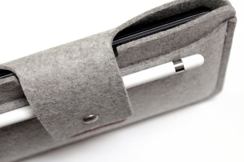 K&ouml;nnte beinhalten: Ein graues Filz-Etui mit einem schwarzen Tablet und einem wei&szlig;en Stift im Inneren. Das Etui hat einen Druckknopfverschluss und einen kleinen Metallknopf.