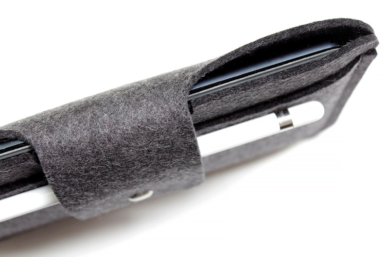 K&ouml;nnte beinhalten: Eine graue Filzh&uuml;lle f&uuml;r ein iPad und einen Apple Pencil. Die H&uuml;lle ist aufgerollt und das iPad und der Pencil sind im Inneren sichtbar.