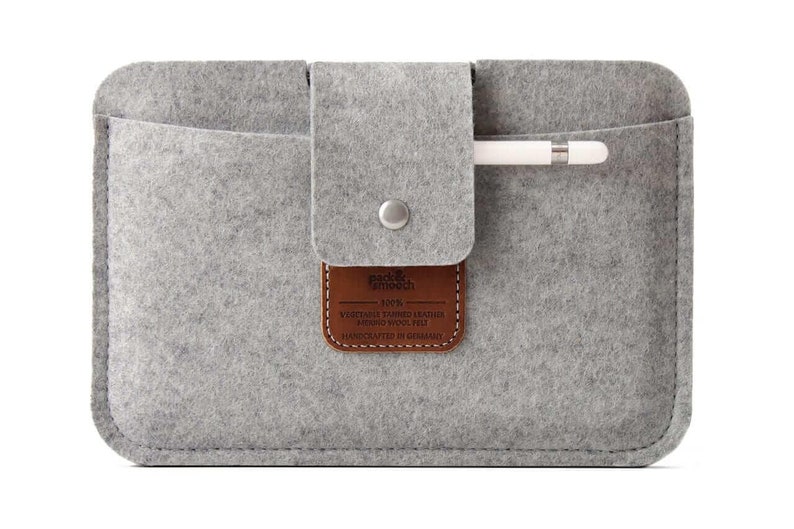 K&ouml;nnte beinhalten: Graue Filz-iPad-H&uuml;lle mit einem braunen Leder-Patch, auf dem "pad & pench 100% VEGETABLE TANNED LEATHER MERINO WOOL FELT HANDCRAFTED IN GERMANY" steht. Die H&uuml;lle hat ein Fach f&uuml;r einen Stift.