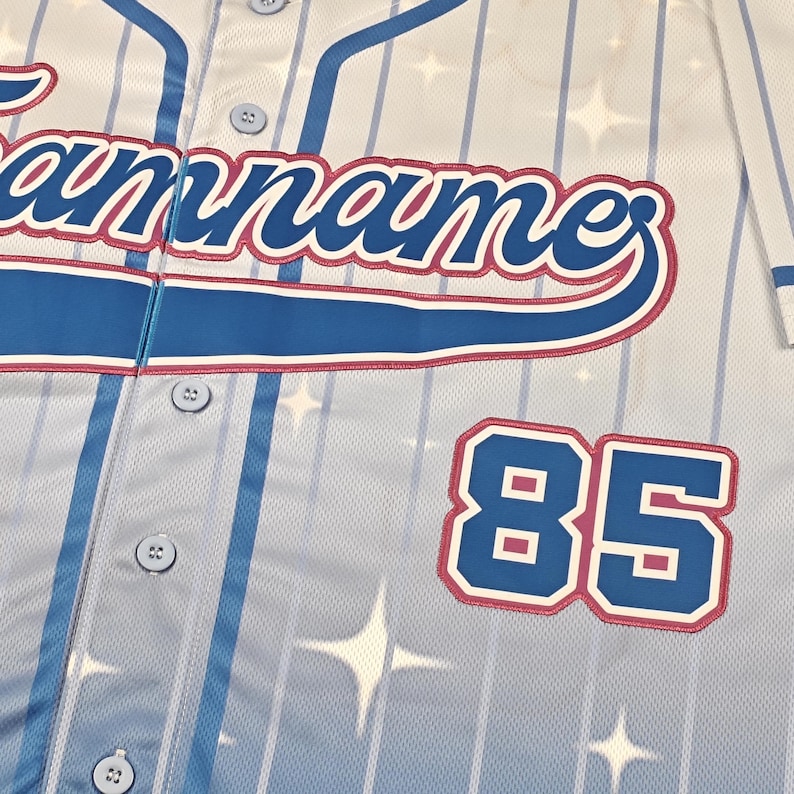 May include: A light blue and white baseball jersey featuring vertical pinstripes and a repeating star pattern. The front displays the text "teamname" in blue script with a pink outline, and the number "85" in blue with a pink outline.