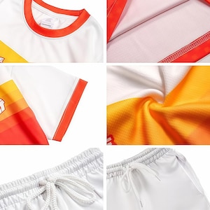 May include: A white t-shirt with an orange crew neck and sleeve trim, featuring a horizontal gradient stripe pattern in yellow and orange. The set includes white shorts with an elastic waistband and a white drawstring cord for a secure fit.