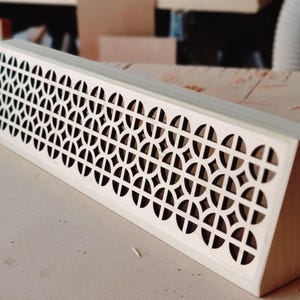 以下が含まれることがあります： 幾何学模様の木製装飾パネル。交差する円と正方形のパターンが特徴です。 パネルは長方形で、端が傾斜しており、家やオフィスの装飾に使用される可能性があります。