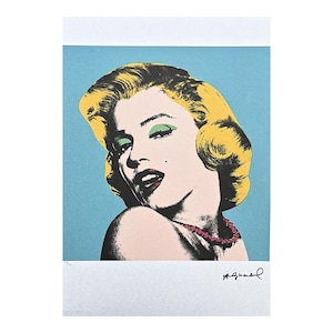 May include: Pop art print of Marilyn Monroe with blonde hair, green eyeshadow, and a pink necklace. The portrait is set against a light blue background. The print includes a signature in the bottom right corner.