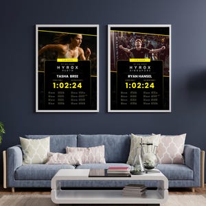 May include: Two framed posters with white borders hang on a dark blue wall. The posters feature athletes and race information. The text "HYROX" is prominent, along with athlete names and race times. The posters are above a blue sofa with decorative pillows.