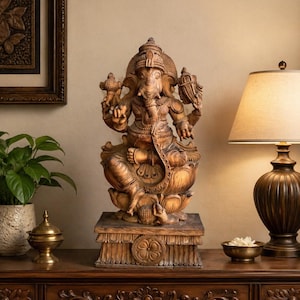 May include: A detailed wooden statue of the Hindu deity Ganesha, seated on a lotus flower. The statue is a warm brown color and is displayed on a carved wooden base. The image is of a home decor item.